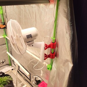 May include: A white fan with a black and white grid pattern is mounted to a green pipe with red clips. The fan is labeled "Hurricane".