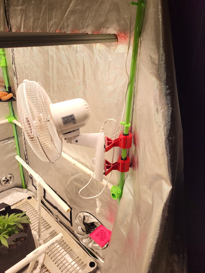 May include: A white fan with a black and white grid pattern is mounted to a green pipe with red clips. The fan is labeled "Hurricane".