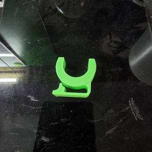 Puede incluir: Un objeto en forma de U de pl&aacute;stico verde brillante con una peque&ntilde;a pesta&ntilde;a en el lateral. El objeto est&aacute; sobre una superficie negra.