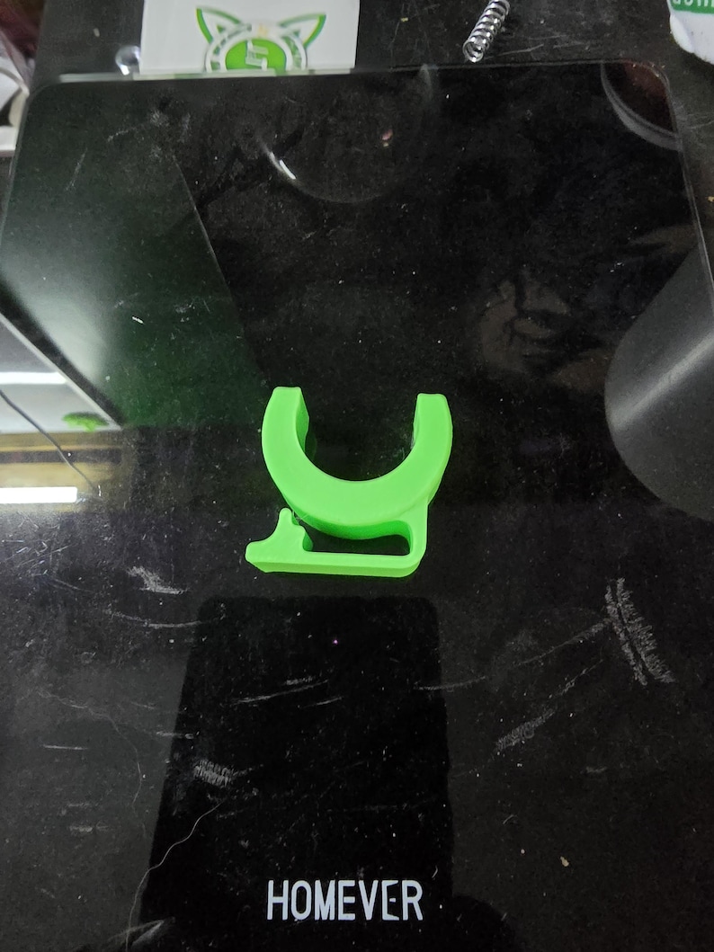Puede incluir: Un objeto en forma de U de pl&aacute;stico verde brillante con una peque&ntilde;a pesta&ntilde;a en el lateral. El objeto est&aacute; sobre una superficie negra.