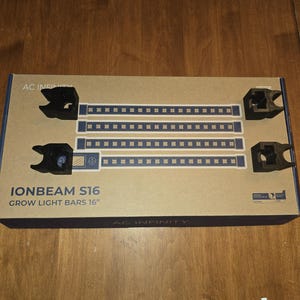 May include: A cardboard box containing two black grow light bars, each with a series of blue lights. The box also includes black mounting brackets. The text "IONBEAM S16 GROW LIGHT BARS 16" is printed on the box.