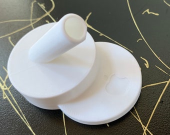 May include: White plastic stand with a round base and a raised platform. The stand has a small, raised tube on the top and an Apple logo on the side.