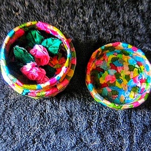 Könnte beinhalten: Zwei bunte runde Boxen mit einem Mosaikmuster. Eine Box ist offen und enthält rosa und grüne Stoffblumen.