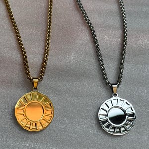 May include: Two necklaces with circular pendants. One necklace is gold-toned, the other is silver-toned. Each pendant features a sunburst design with a central circle. The chains are a wheat style.