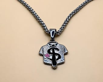 May include: A silver-toned metal pendant shaped like a collared shirt with a tie, featuring a prominent black dollar sign symbol and a small pink star accent. The pendant hangs from a matching silver-toned wheat chain necklace with a textured link design.