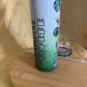 以下が含まれることがあります： スターバックスのデザインが施された、背の高い断熱タンブラー。タンブラーは、スターバックスのロゴとドリンクのカスタマイズオプションを備えた、グラデーションの緑色の背景が特徴です。蓋とストローが含まれています。