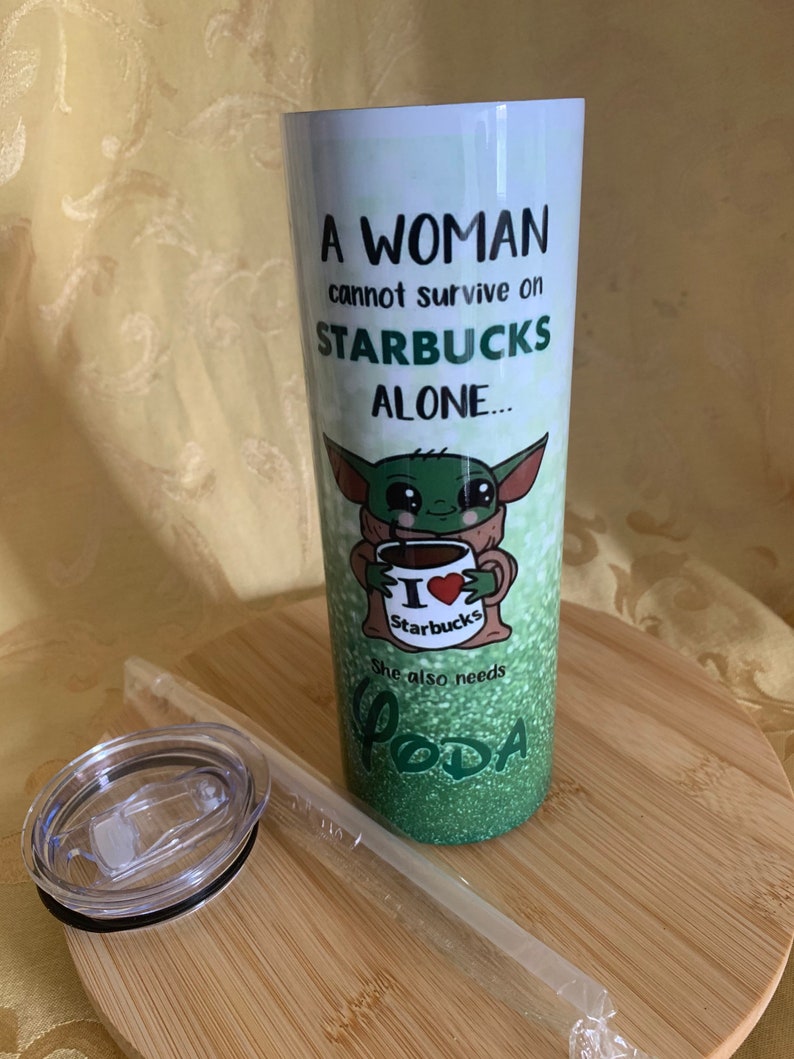 以下が含まれることがあります： 緑色のグリッターデザインと「A WOMAN cannot survive on STARBUCKS ALONE... She also needs YODA」の文字が入った白いタンブラー。スターバックスのカップを持ったベビーヨーダの漫画の画像が特徴です。透明な蓋とストローが含まれています。