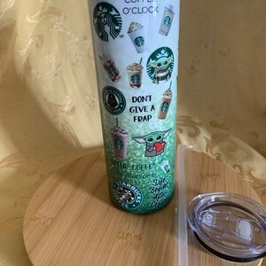 以下が含まれることがあります： スターバックスをテーマにした白いタンブラー。スターバックスのロゴ、さまざまなコーヒー、そして「Coffee O'Clock」というフレーズが特徴です。デザインには、ベビーヨーダのグラフィックと「Don't Give a Frap」というテキストが含まれています。