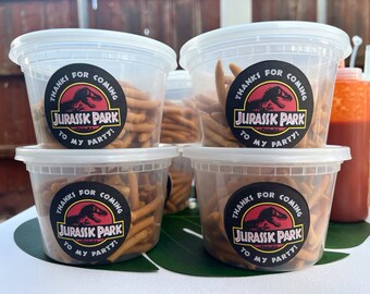 Puede incluir: Cuatro recipientes de plástico transparente llenos de palitos de pretzel marrones. Cada recipiente tiene una pegatina en blanco y negro con un gráfico de dinosaurio y el texto "¡Gracias por venir a mi fiesta de Jurassic Park!"