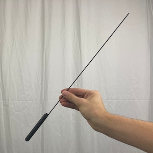 May include: A slender, black rod with a rounded, thicker handle. The rod is held in a person's hand against a white backdrop. The handle appears to be made of a solid, matte material.