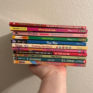 Puede incluir: Una pila de libros de bolsillo, incluyendo títulos como "Lizzie McGuire", "Full House", "True Blue", "Finding Meridian", "High School Musical", "Camp Rock", "Goosebumps", "iCarly" y "R.L. Stine".