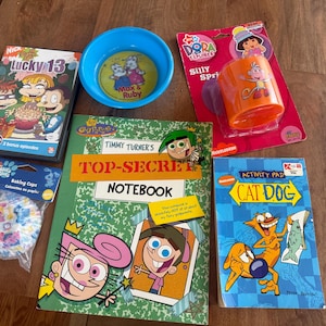 May include: A collection of Nickelodeon merchandise including a Rugrats Lucky 13 DVD, a blue Max & Ruby bowl, a Dora the Explorer Silly Spring toy, a pack of Blue's Clues baking cups, a Fairly OddParents Top-Secret Notebook, and a CatDog activity pad.