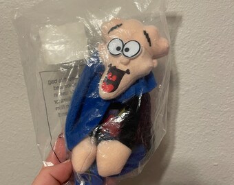 Peut inclure: Un jouet en peluche représentant un personnage de dessin animé avec une cape bleue et la bouche grande ouverte. Le personnage a de grands yeux et une expression surprise.