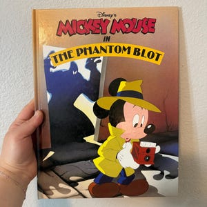 Puede incluir: Un libro vintage de Disney Mickey Mouse titulado "The Phantom Blot". La portada presenta a Mickey Mouse con gabardina y sombrero amarillos, sosteniendo una cámara roja. El título está en letras rojas y amarillas.