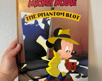 Op de afbeelding: Een vintage Disney's Mickey Mouse boek getiteld "The Phantom Blot". De cover toont Mickey Mouse in een gele trenchcoat en hoed, met een rode camera. De titel staat in rode en gele letters.