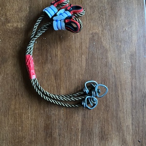 May include: Two green ropes with red and black accents are tied together with a red tape. The ropes have metal loops on the ends.