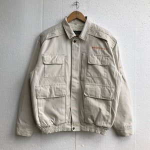 May include: A beige utility jacket with multiple pockets and a drawstring waist. The jacket has the text "富士コカ・コーラ" embroidered on the front.
