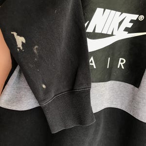 Pu&ograve; includere: Felpa Nike Air nera e grigia. Il logo Nike &egrave; bianco, con la scritta "AIR" sotto. La manica presenta delle macchie.