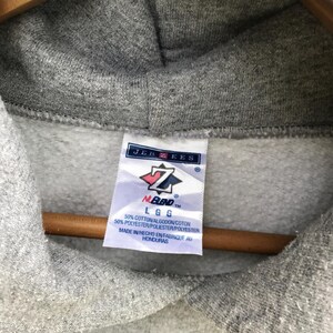 May include: Gray hooded sweatshirt with a Jerzees tag. The tag has a red and white logo with the text "NUBlend" and "LGG". The tag also includes the text "50% Cotton/Algodon/Coton 50% Polyester/Poliester/Polyester Made in/Hecho en/Fabrique au Honduras".