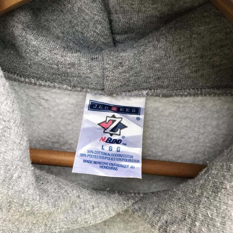May include: Gray hooded sweatshirt with a Jerzees tag. The tag has a red and white logo with the text "NUBlend" and "LGG". The tag also includes the text "50% Cotton/Algodon/Coton 50% Polyester/Poliester/Polyester Made in/Hecho en/Fabrique au Honduras".