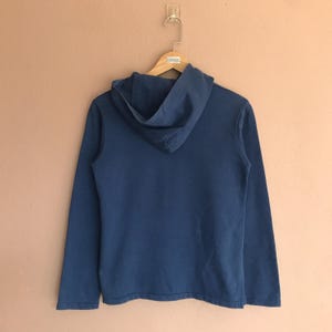 May include: A solid blue hoodie with a hood and long sleeves hangs on a wooden hanger. The hoodie is made of a soft material and is displayed against a neutral background. The back of the hoodie is visible.
