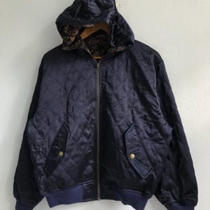 Pu&ograve; includere: Una giacca trapuntata blu navy con chiusura a zip e cappuccio. La giacca ha due tasche sul davanti e un elastico in vita blu navy.