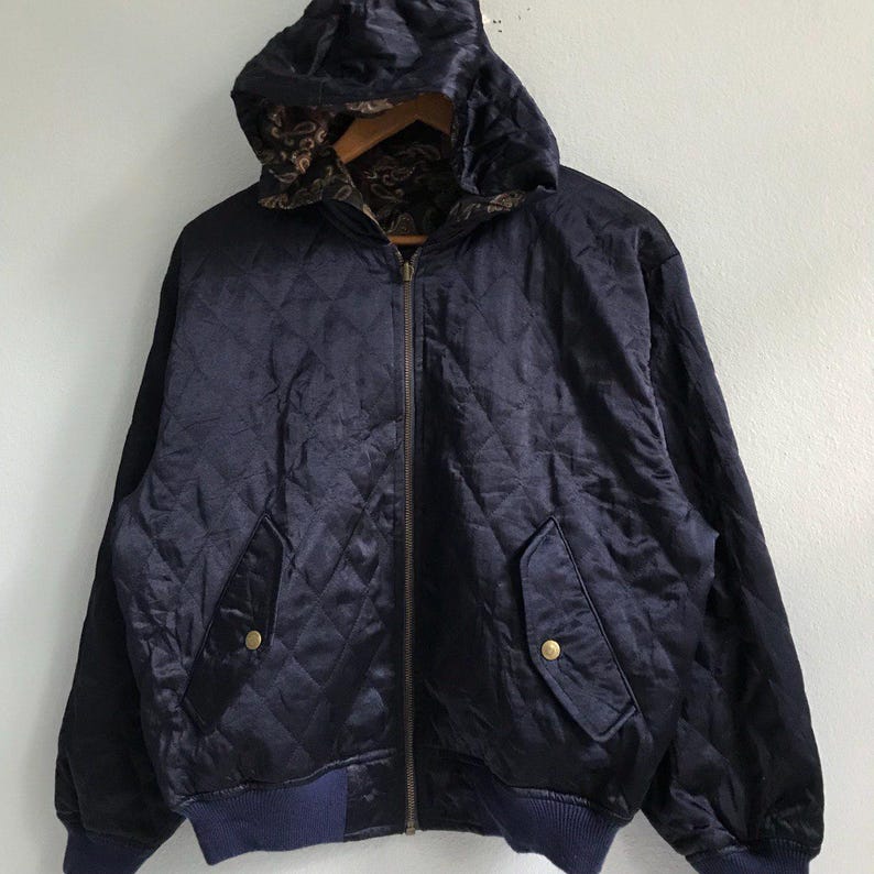 Pu&ograve; includere: Una giacca trapuntata blu navy con chiusura a zip e cappuccio. La giacca ha due tasche sul davanti e un elastico in vita blu navy.