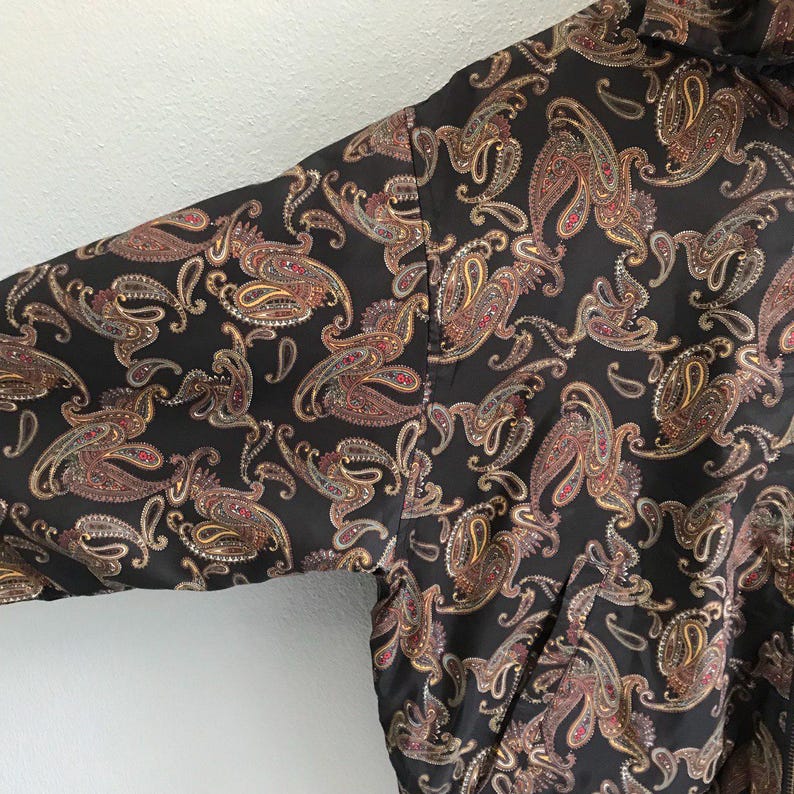 Pu&ograve; includere: Una giacca nera con motivo paisley e chiusura a zip. La giacca ha una lucentezza discreta e un design classico.