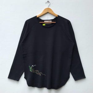 May include: Black long-sleeve shirt with a green and white dragon graphic on the left side. The shirt has a crew neck and a relaxed fit.