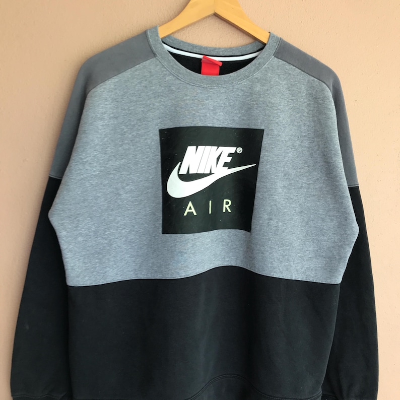 Pu&ograve; includere: Una felpa Nike Air grigia, nera e bianca. La felpa ha un grande quadrato nero con il logo Nike e "AIR" stampato in bianco. La parte superiore della felpa &egrave; grigia e la parte inferiore &egrave; nera.