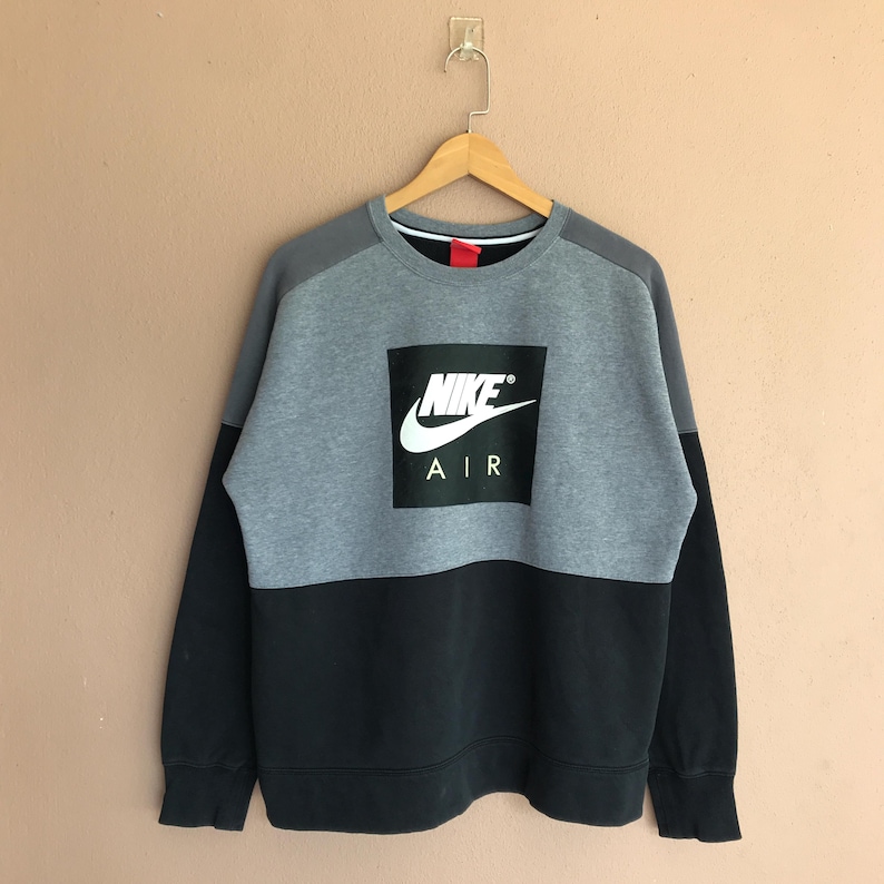 Pu&ograve; includere: Una felpa Nike Air grigia e nera. La met&agrave; superiore della felpa &egrave; grigia, con maniche nere e la met&agrave; inferiore della felpa &egrave; nera. Il logo Nike &egrave; in un quadrato nero sul davanti.