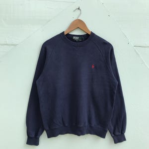 May include: A navy blue sweatshirt with a small red polo player logo on the left chest. The sweatshirt has a crew neck and long sleeves.