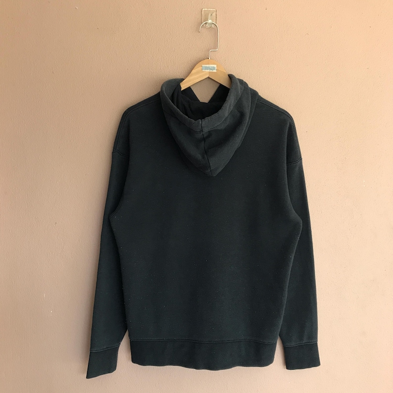 May include: A black hoodie hanging on a wooden hanger. The sweatshirt features a drawstring hood and long sleeves. The back view of the hoodie shows the hood and the main body of the garment.