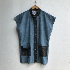 May include: A sleeveless blue jacket with black trim and two front pockets. The jacket has a mandarin collar and is buttoned down the front. The interior collar lining features a white and blue floral pattern. The jacket is hanging on a wooden hanger.