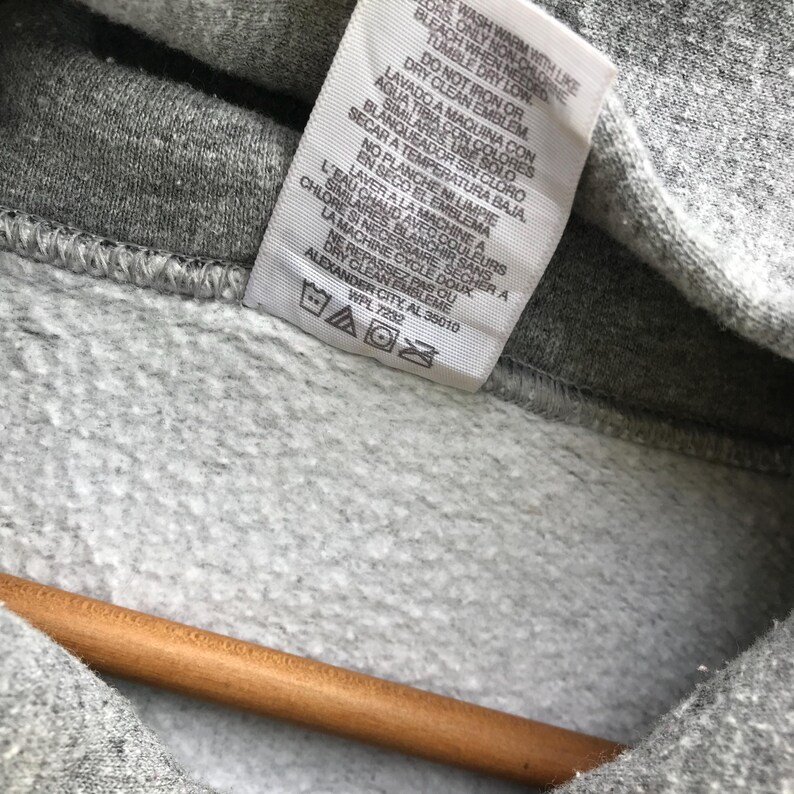 May include: A gray hooded sweatshirt with a white care tag. The tag has instructions for washing, drying, and bleaching the garment. The tag also includes the text "WPL 7232" and "ALEXANDER CITY, AL 35010".
