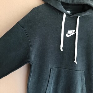 May include: Black Nike hoodie with a white drawstring and the Nike logo on the chest. The hoodie features a front pocket and a hood. The fabric appears to be a soft, comfortable material.