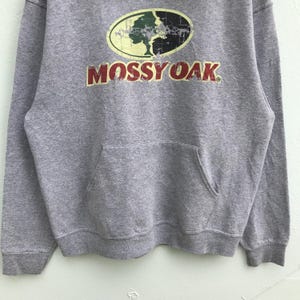May include: Gray hooded sweatshirt with a Mossy Oak logo featuring a green tree and the words "Mossy Oak" in red.