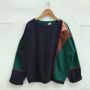 Könnte beinhalten: Ein dunkelblauer und grüner Patchwork-Pullover mit roten Nähten. Der Pullover hat eine lockere Passform und einen runden Ausschnitt.