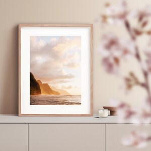 May include: A framed photograph of a beach scene with a rocky coastline and a golden sunset sky. The water is calm and the sky is filled with fluffy clouds.