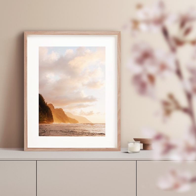 May include: A framed photograph of a beach scene with a rocky coastline and a golden sunset sky. The water is calm and the sky is filled with fluffy clouds.