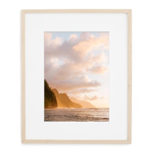 May include: A photograph of a beach scene with a rocky coastline and a cloudy sky. The sun is setting, casting a warm glow on the water and the clouds. The beach is empty, with only the waves crashing on the shore.