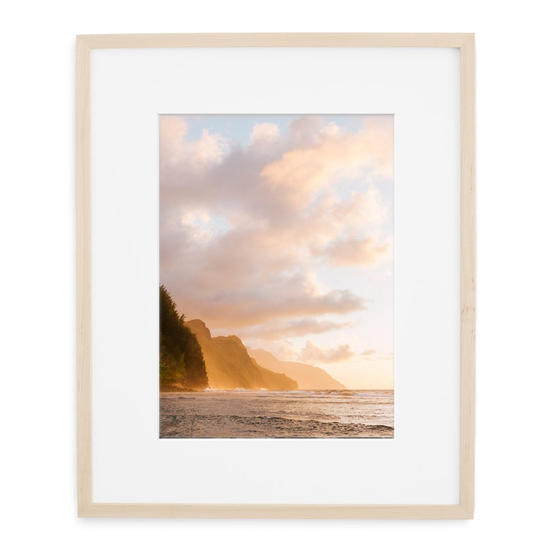May include: A photograph of a beach scene with a rocky coastline and a cloudy sky. The sun is setting, casting a warm glow on the water and the clouds. The beach is empty, with only the waves crashing on the shore.