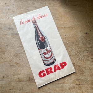 May include: A vintage paper bag with a wine bottle illustration. The bag features the words "le vin de classe" in red script at the top and the word "GRAP" in large red letters at the bottom. The bottle is black and red.