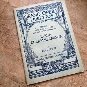 May include: A vintage book cover for the opera Lucia di Lammermoor by Donizetti. The cover features an ornate design with a title card and the publisher's name, Oliver Ditson Company.
