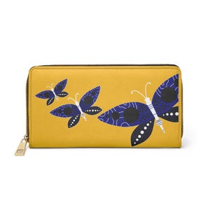 May include: Mustard yellow zippered wallet featuring a butterfly design in navy blue and white. The butterflies have intricate wing patterns and are arranged across the front of the wallet. The wallet has a gold-colored zipper pull.