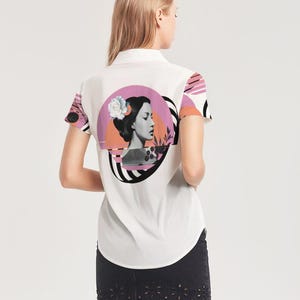 May include: White button-up shirt with a graphic design on the back featuring a woman's profile, a flower, and abstract shapes in pink, black, and orange. The short sleeves have a pink and white pattern.