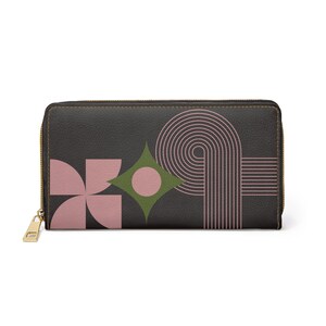 Könnte beinhalten: Eine dunkelgraue Geldbörse mit goldenem Reißverschluss und geometrischem Design. Das Design umfasst rosa und grüne Formen, darunter eine Blume, eine Raute und ein Kreis, sowie rosa gebogene Linien.