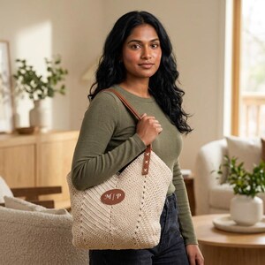 Può includere: Una borsa tote all'uncinetto color beige con una toppa ovale in pelle marrone che riporta il monogramma bianco M | P. La borsa presenta manici in pelle marrone fissati con visibili cuciture a croce bianche sugli angoli superiori.