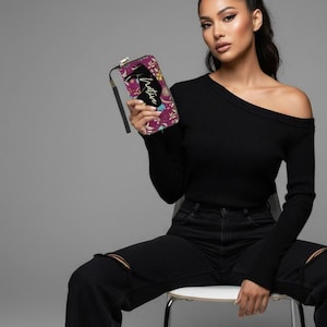 May include: A rectangular clutch with a wrist strap. The clutch features a floral pattern in shades of purple, yellow, and white. The word "Native" is written in a cursive font on the front of the clutch. The clutch has a black silhouette design.