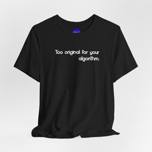 Puede incluir: Camiseta negra con el texto blanco "Too original for your algorithm." La camiseta de manga corta tiene cuello redondo. La tela parece suave y ligeramente arrugada. Un pequeño logotipo circular azul es visible cerca del cuello.